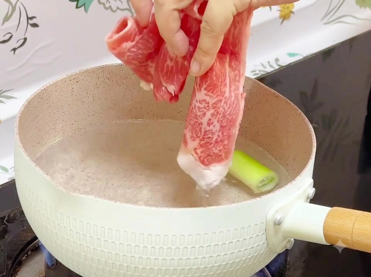 長ねぎの入った沸騰したお湯の入った鍋に、冷凍の牛肉ロールを入れているところ
