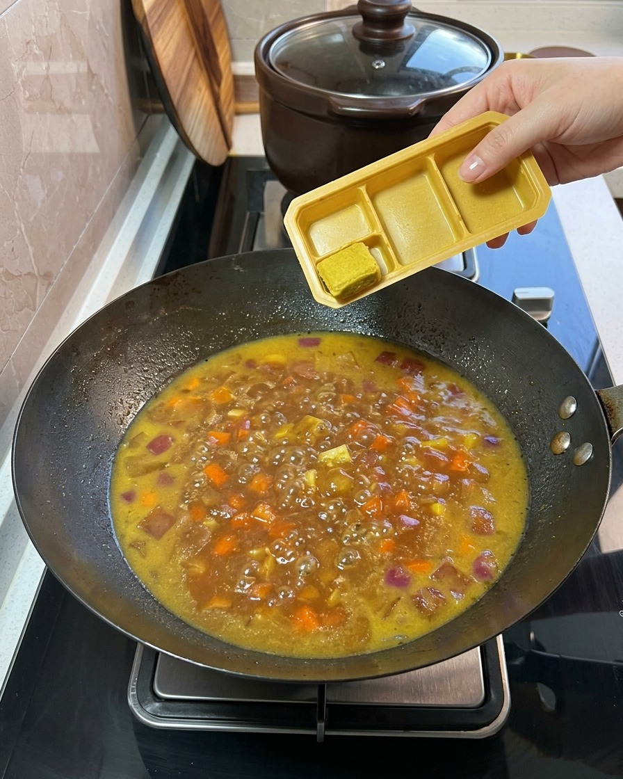 煮込んでいる野菜とスープの中に、プラスチックトレイから固形のカレールーを加えている様子。