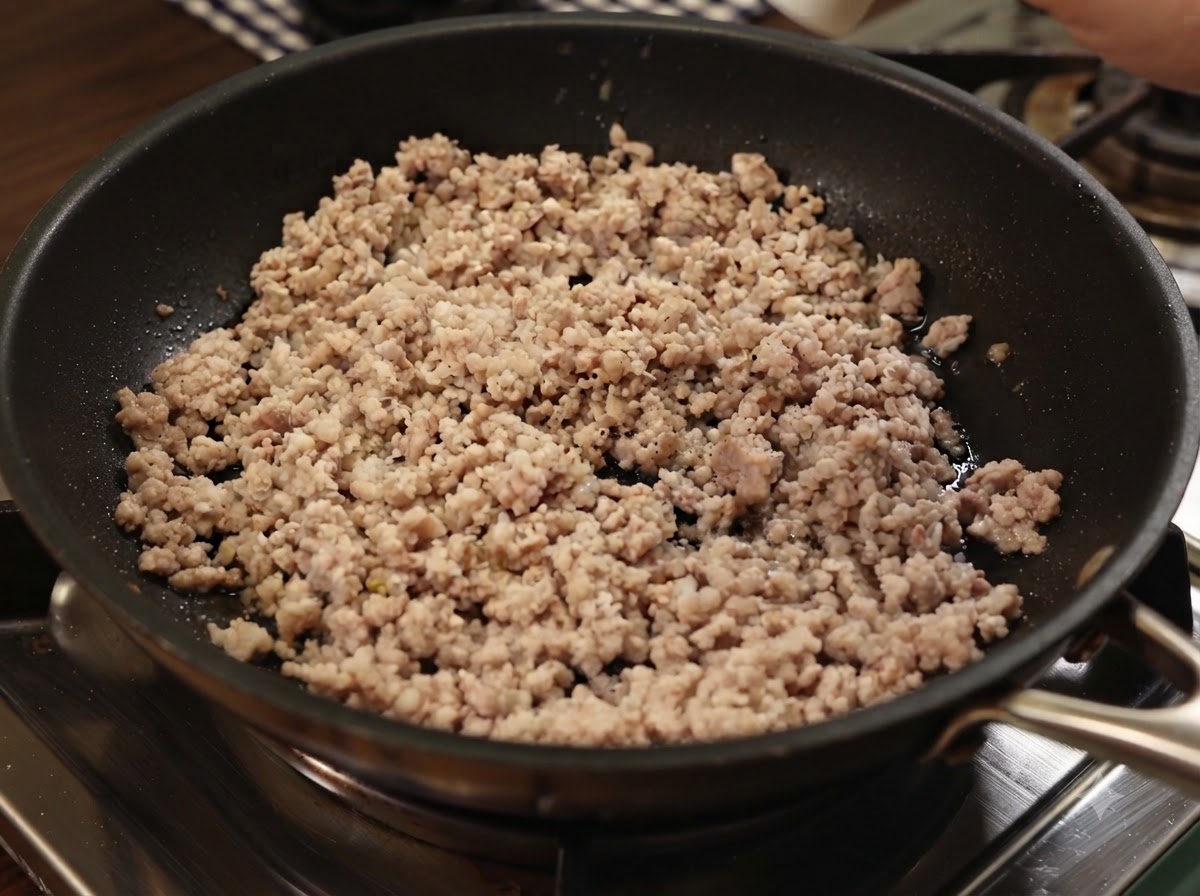 フライパンで炒めた豚ひき肉に黒こしょうと海塩をふりかけている様子。