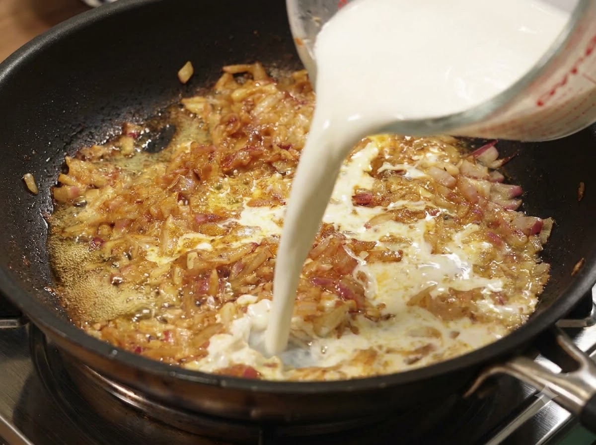 計量カップから、玉ねぎとカレーが煮込まれたフライパンに牛乳を注ぎ入れている様子。
