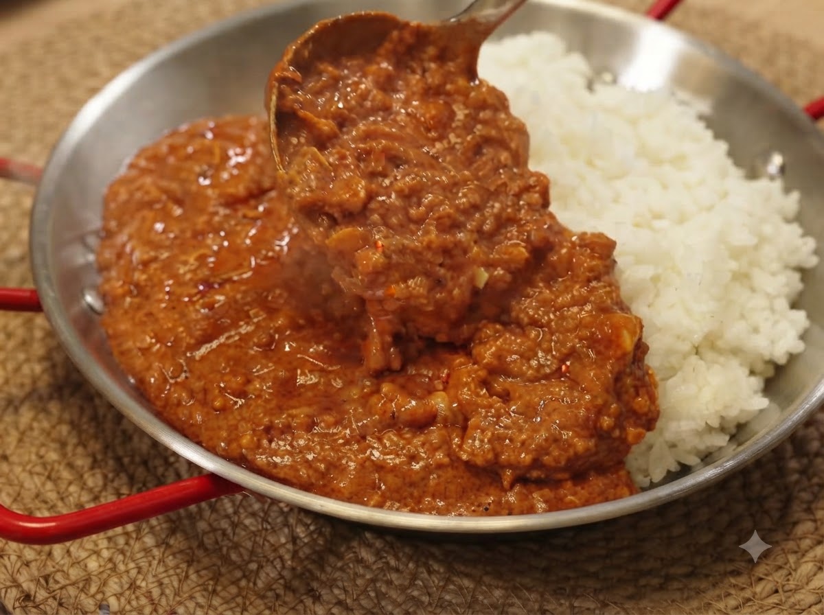 おたまですくった濃厚なポークキーマカレーソースを、白ご飯の上にたっぷりかけている様子。