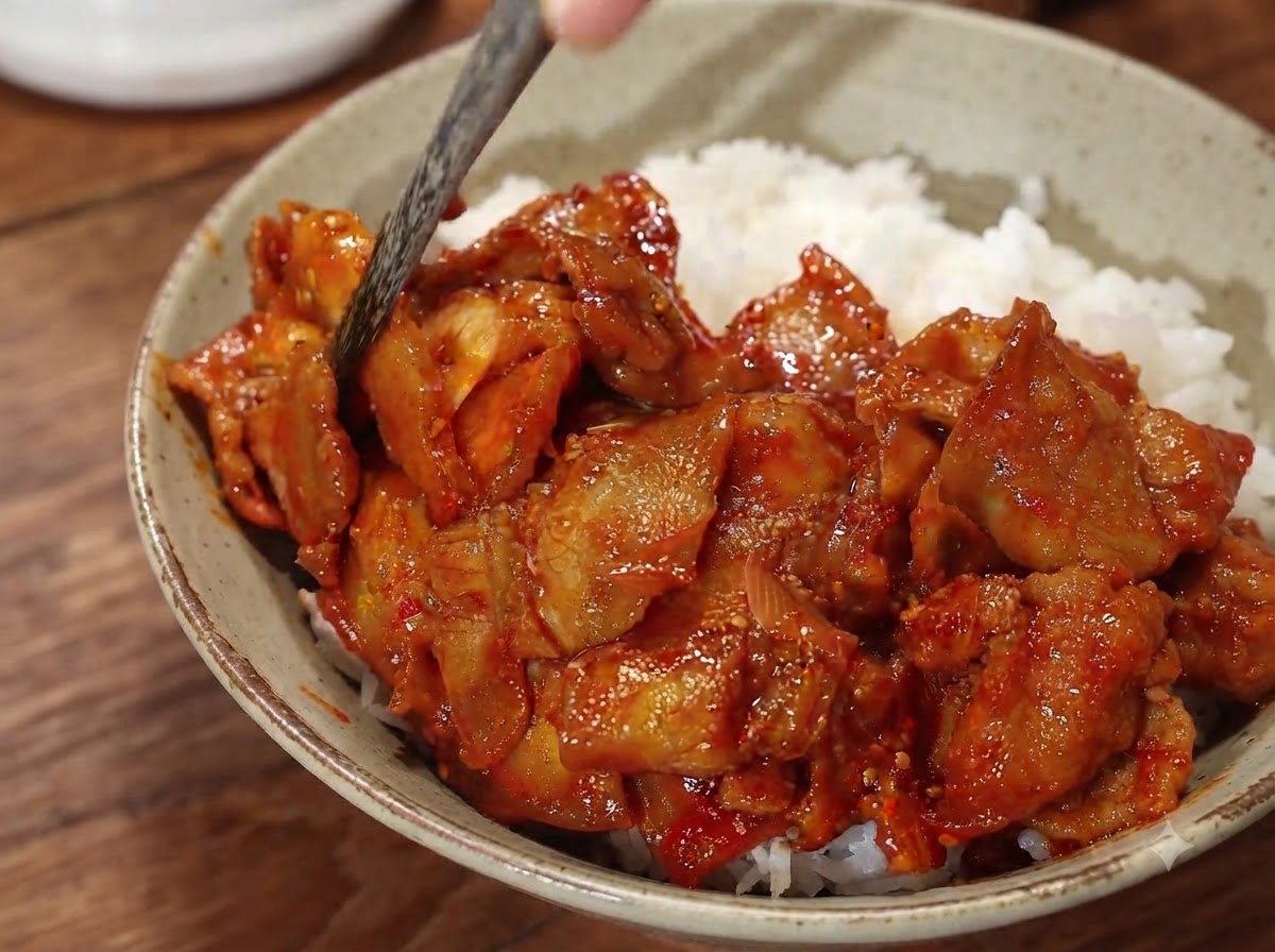 水にさらしたスライス玉ねぎをトッピングし、箸で盛り付けを整えているピリ辛豚肉丼のクローズアップ