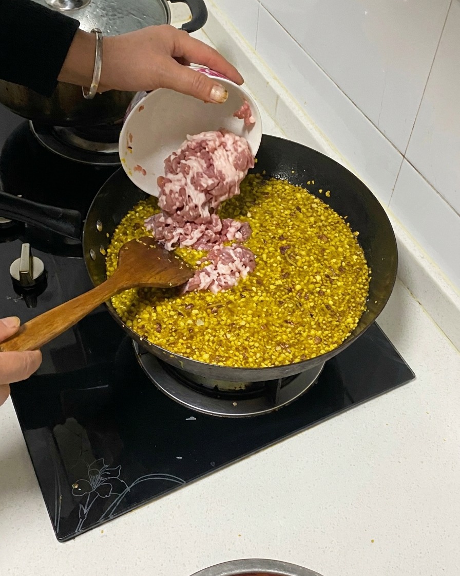 炒めた香味野菜と油の入った中華鍋に、小さなボウルからダイス状の豚バラ肉を投入している様子