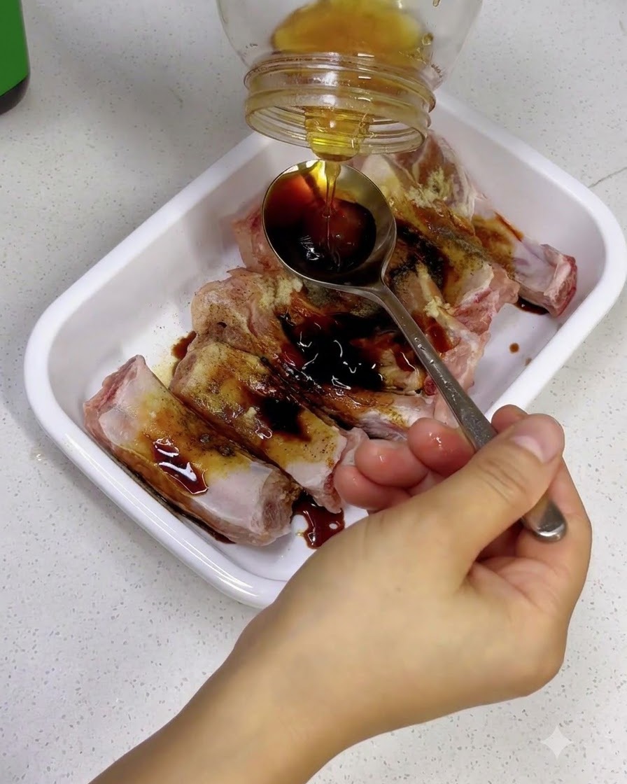 味付けしたスペアリブに、スプーンを使って黄金色のはちみつをかけている様子。