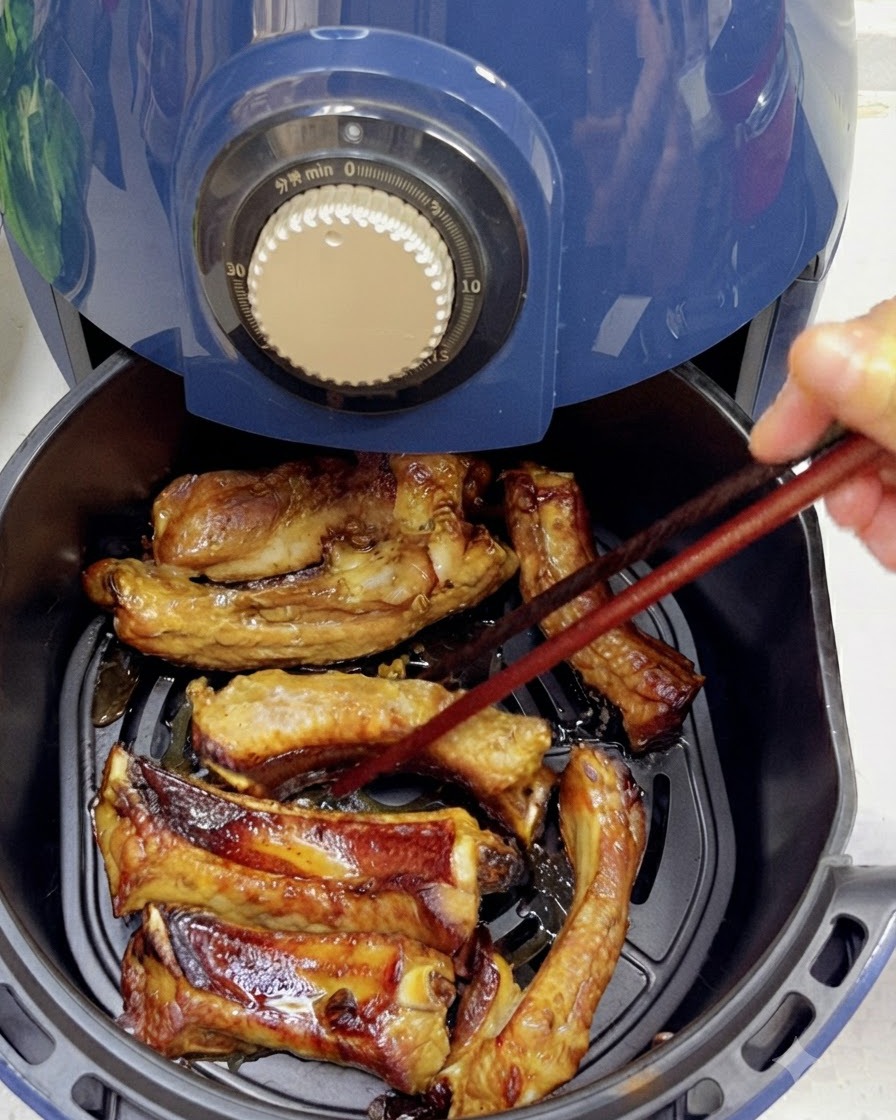 こんがりと焼き色がつき始めたスペアリブを、箸を使って裏返している様子。