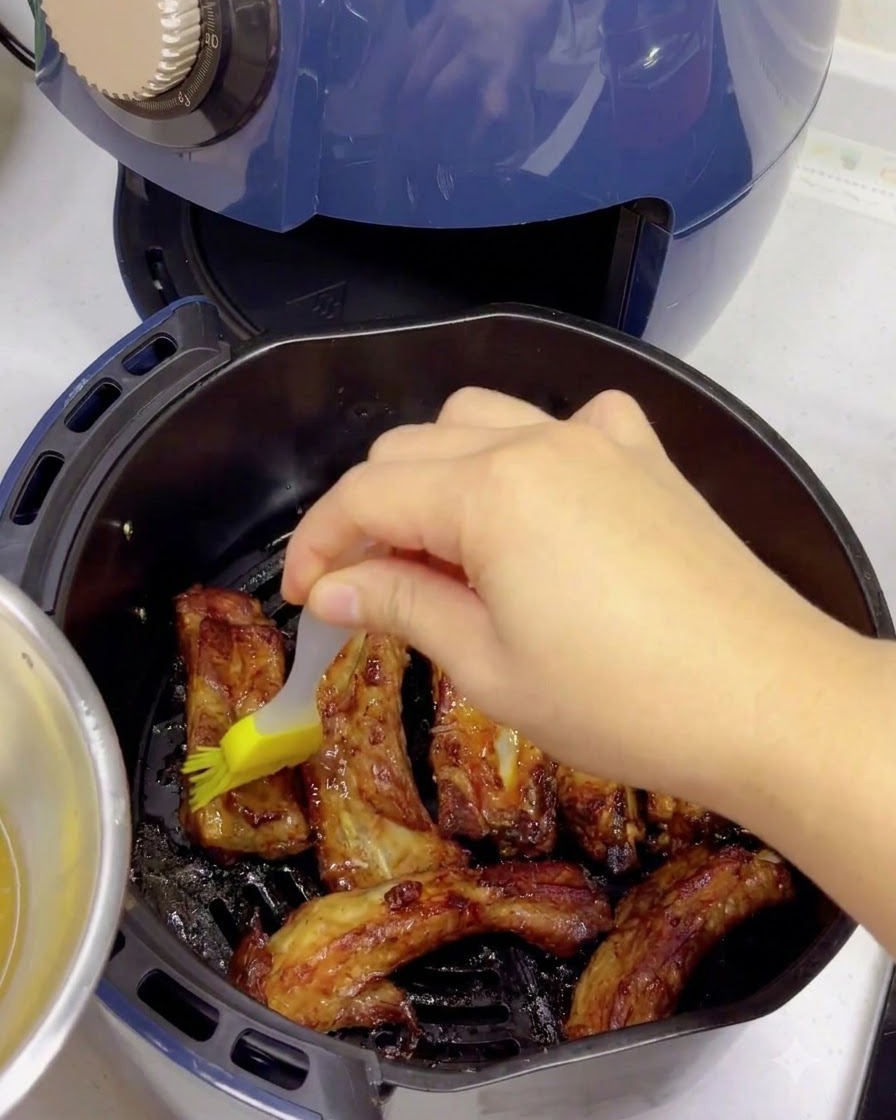 焼き上がったスペアリブに、シリコンハケを使ってはちみつ水を塗っている様子。