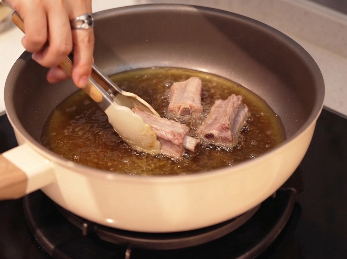 トングを使って熱した油で揚げ焼きにされる豚スペアリブ。