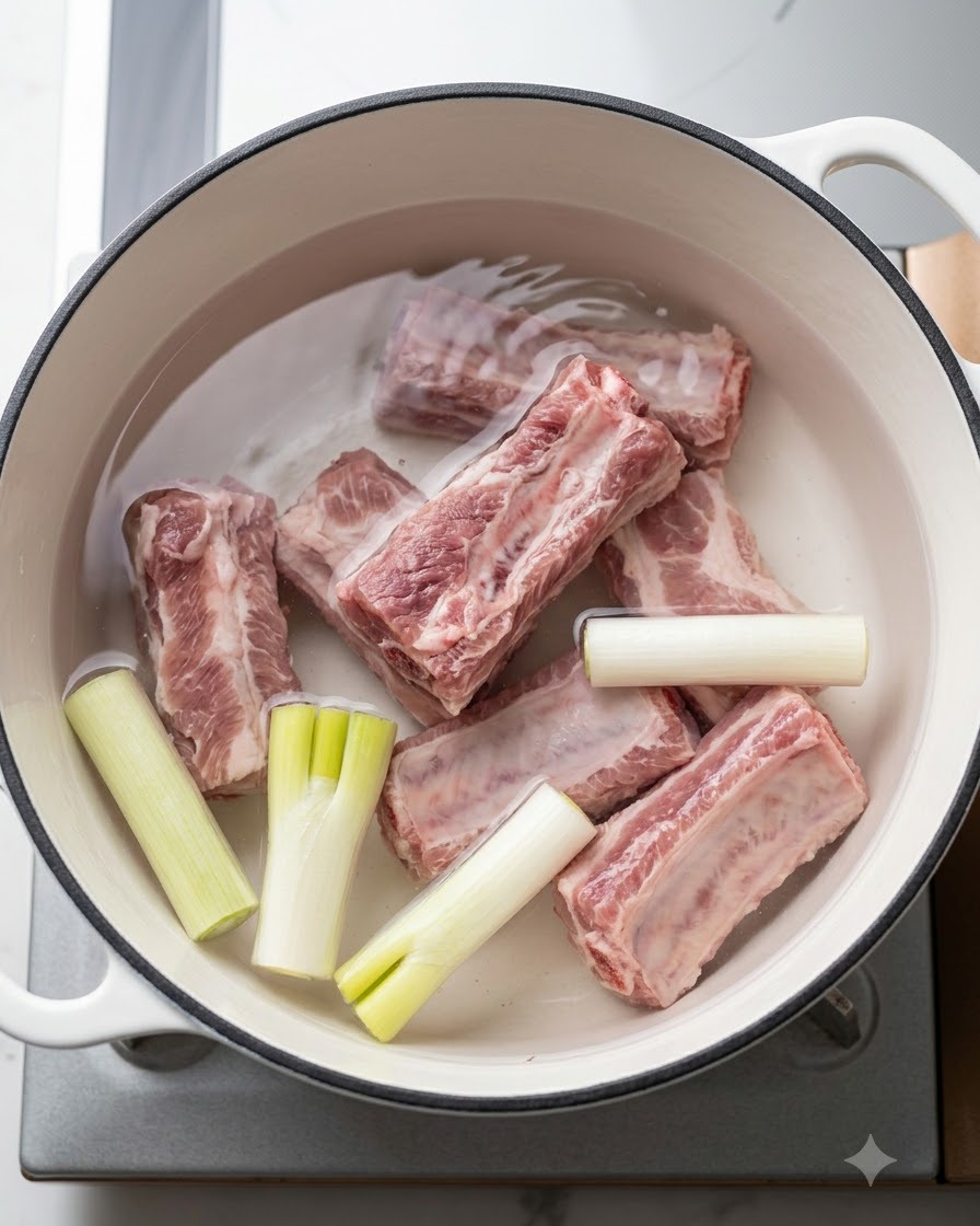 茹でる前に、青ネギや香味野菜と一緒に冷水を入れた鍋に入っている生の豚スペアリブ。