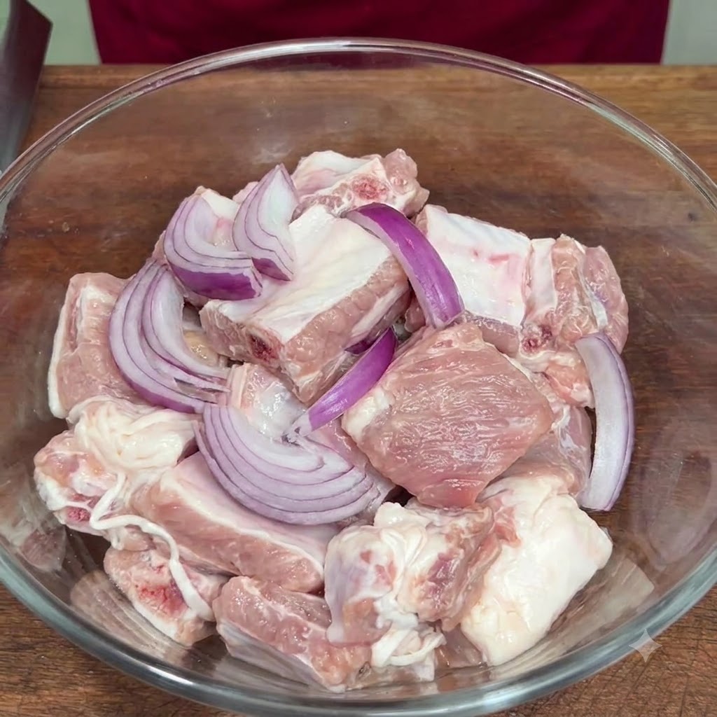 ガラスボウルに入った豚肉に、スライスした赤玉ねぎや調味料を加えている様子。