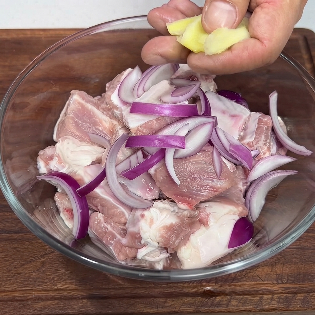 豚肉と赤玉ねぎが入ったガラスボウルに生姜スライスを入れている様子。