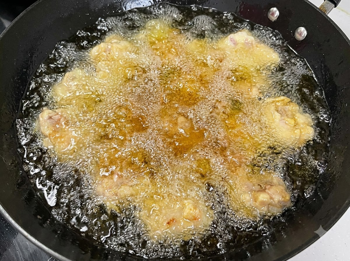 複数の豚肉が黒い中華鍋の中でグツグツと音を立てて揚げられている様子。
