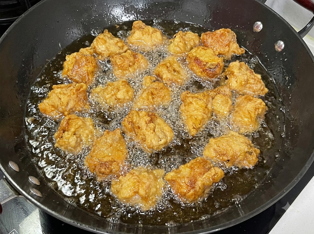 衣のついた豚肉の塊が、泡立つ油の入った黒い中華鍋で揚げられている様子。