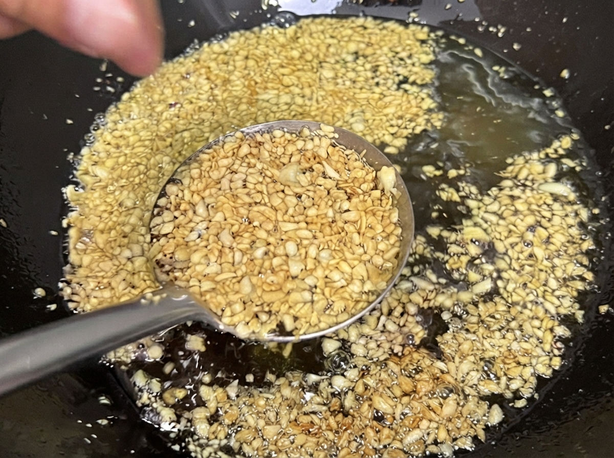 中華鍋の油の中でにんにくが揚げられ、サクサクの薄い黄金色に変わっていく様子。