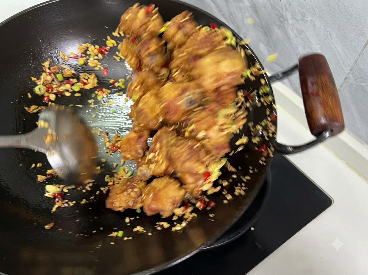 豚肉、唐辛子、にんにくが中華鍋の中でお玉を使って均一に混ぜ合わされている様子。