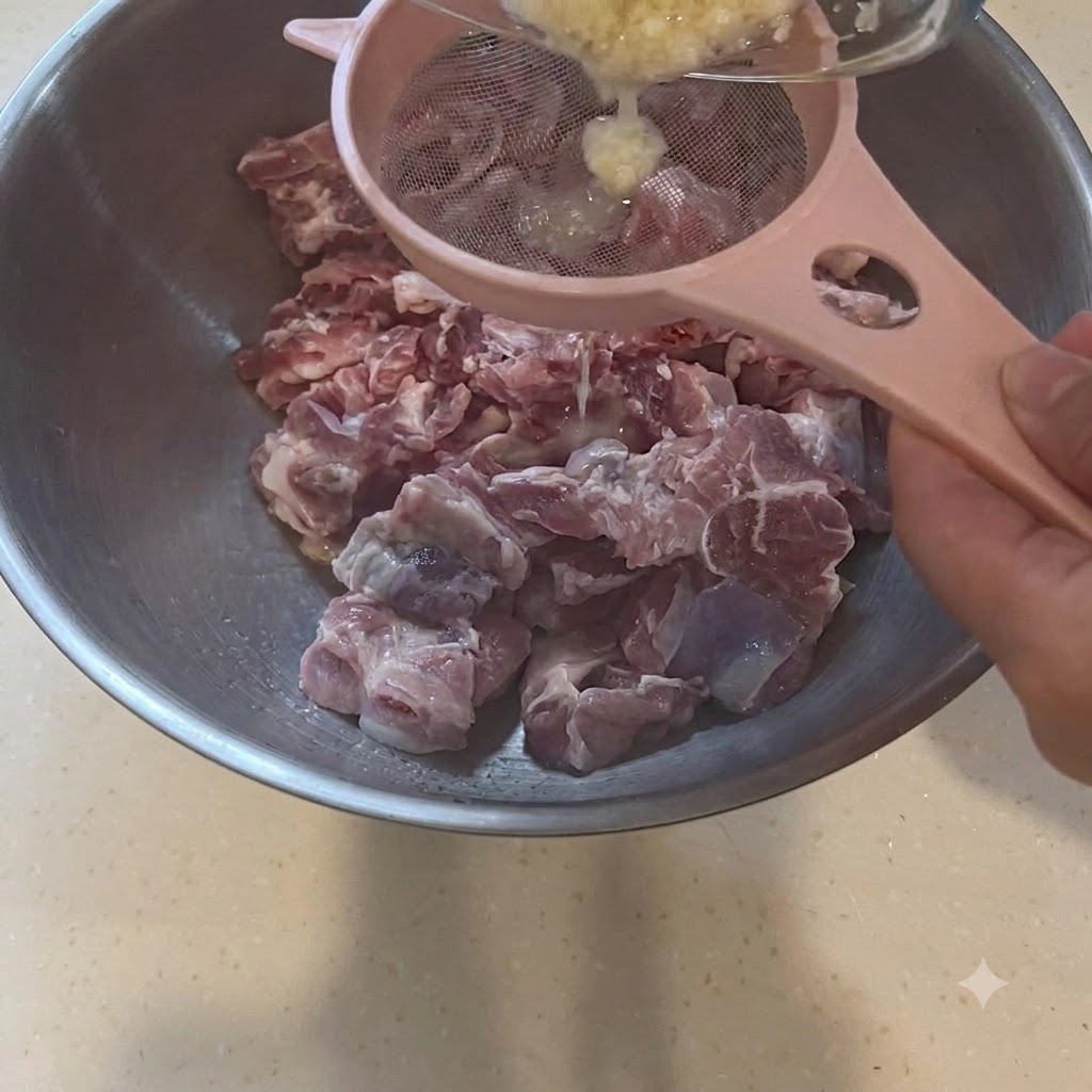 生豚肉の入った大きなボウルの上で、ピンク色のザルを使ってにんにくペーストを濾している様子。