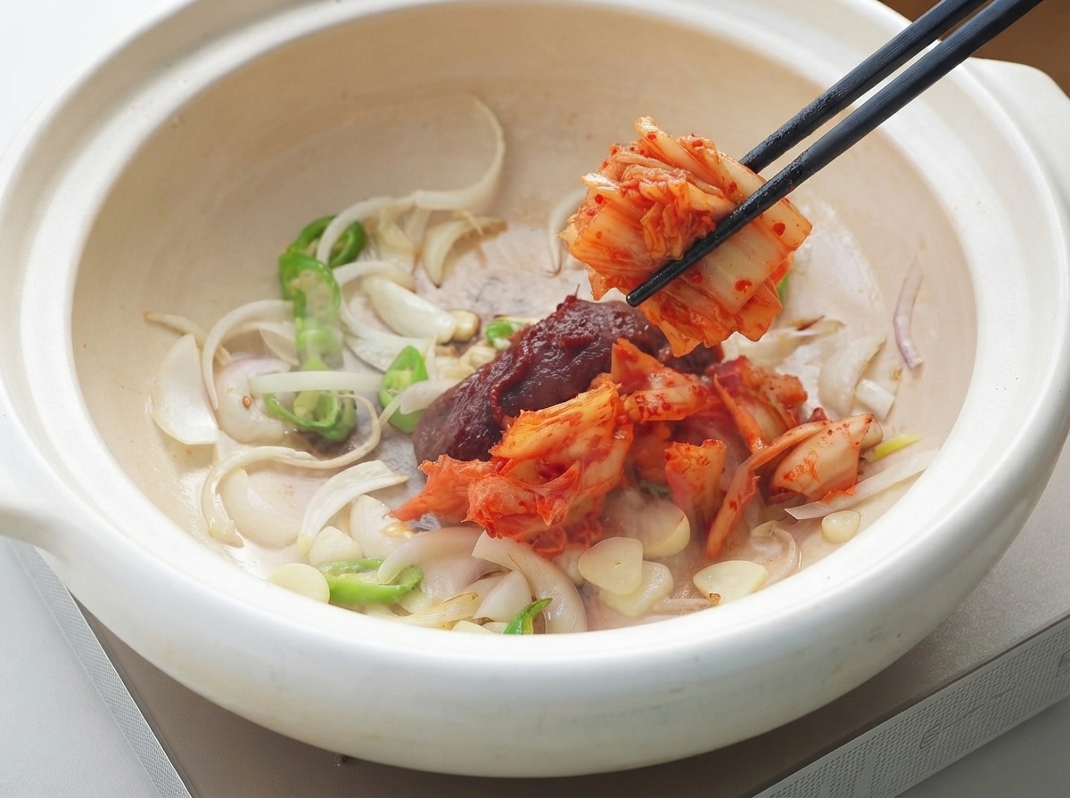 箸を使って、炒めた薬味が入った鍋に韓国産コチュジャンとキムチを加えている様子。