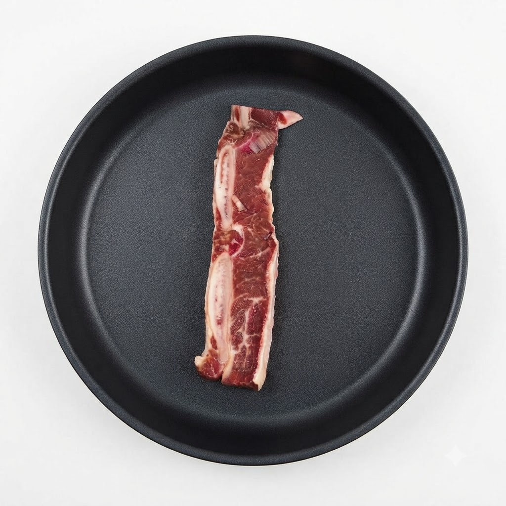 暗い色のフライパンに味付けされた牛カルビの肉が1枚置かれている様子。