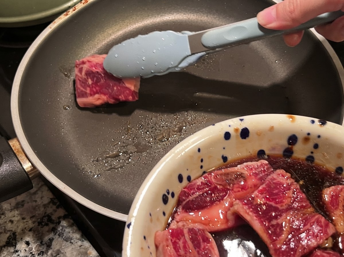 トングを使って、熱したフライパンにマリネした牛カルビの肉片を入れている様子。