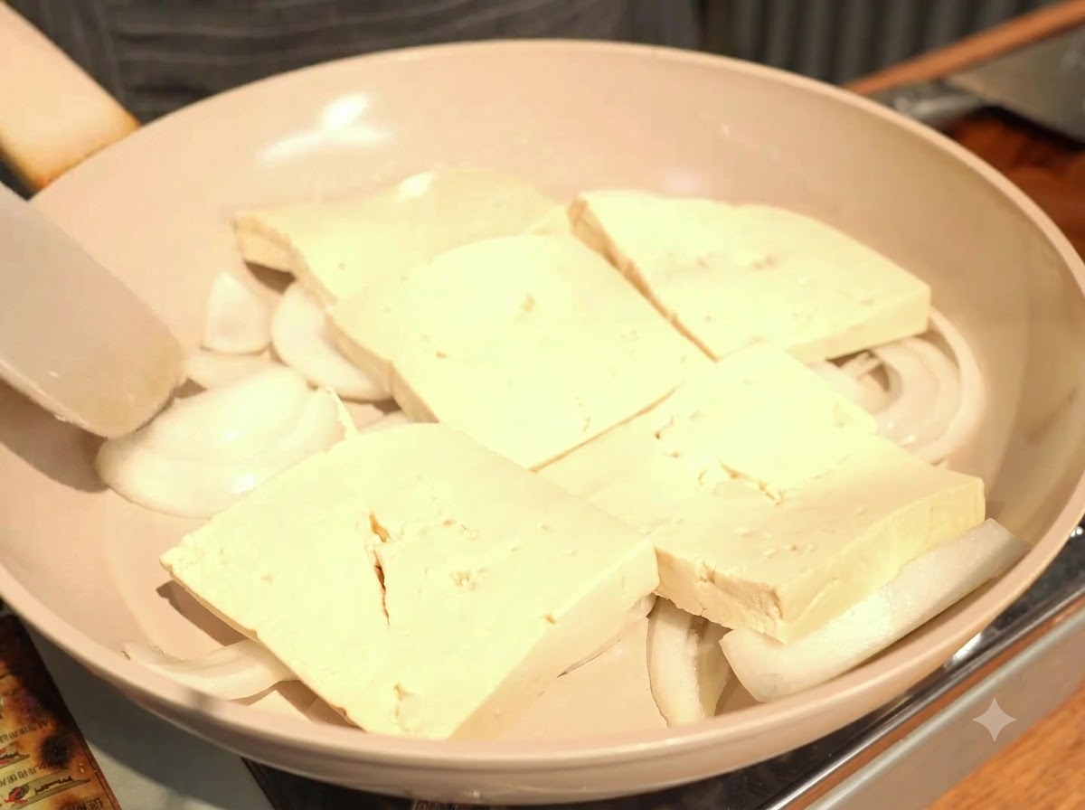 玉ねぎの上に、厚切りの豆腐を少しずつ重ねながら1列に並べている様子。