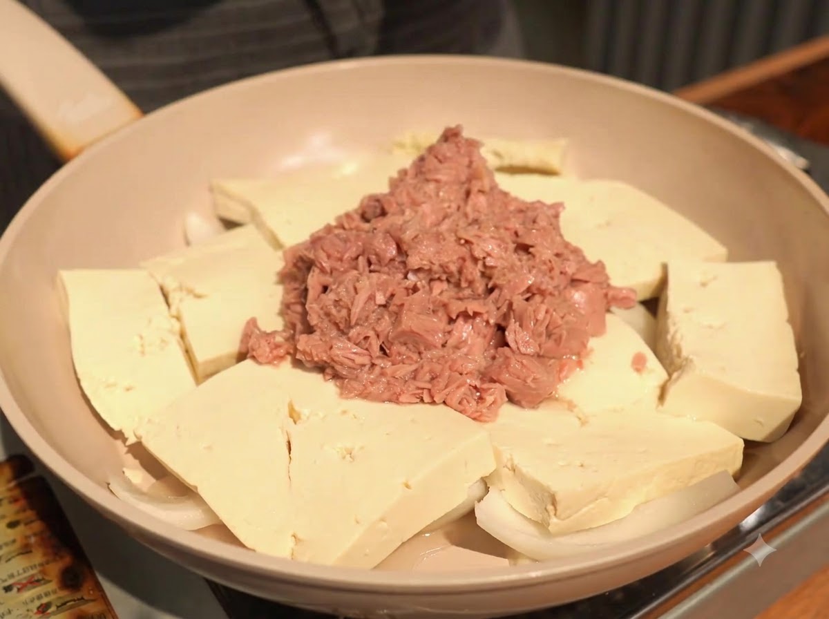 ツナの横の豆腐の上に、スプーン一杯のおろしニンニクを鍋に加えている様子。
