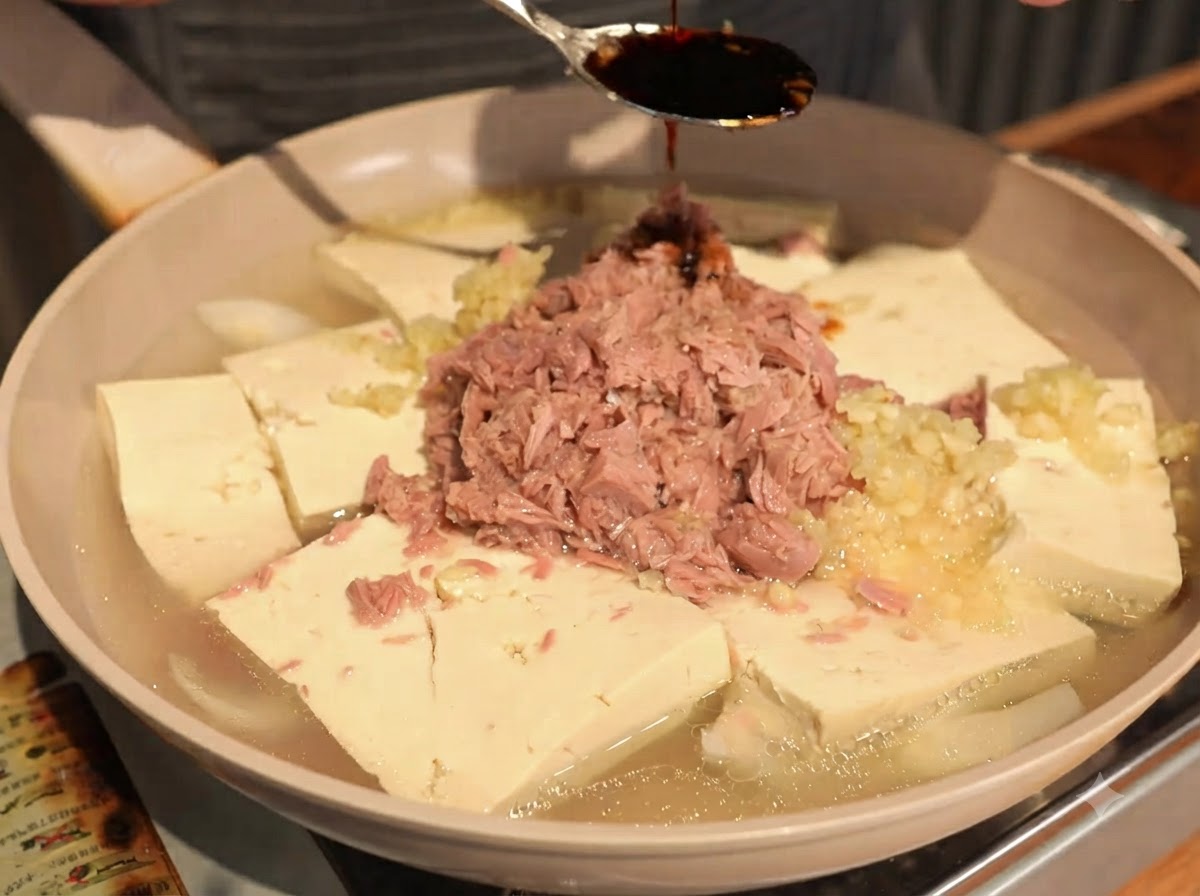 スプーンを使って、ツナと豆腐の上にスープ用醤油を回しかけている様子。