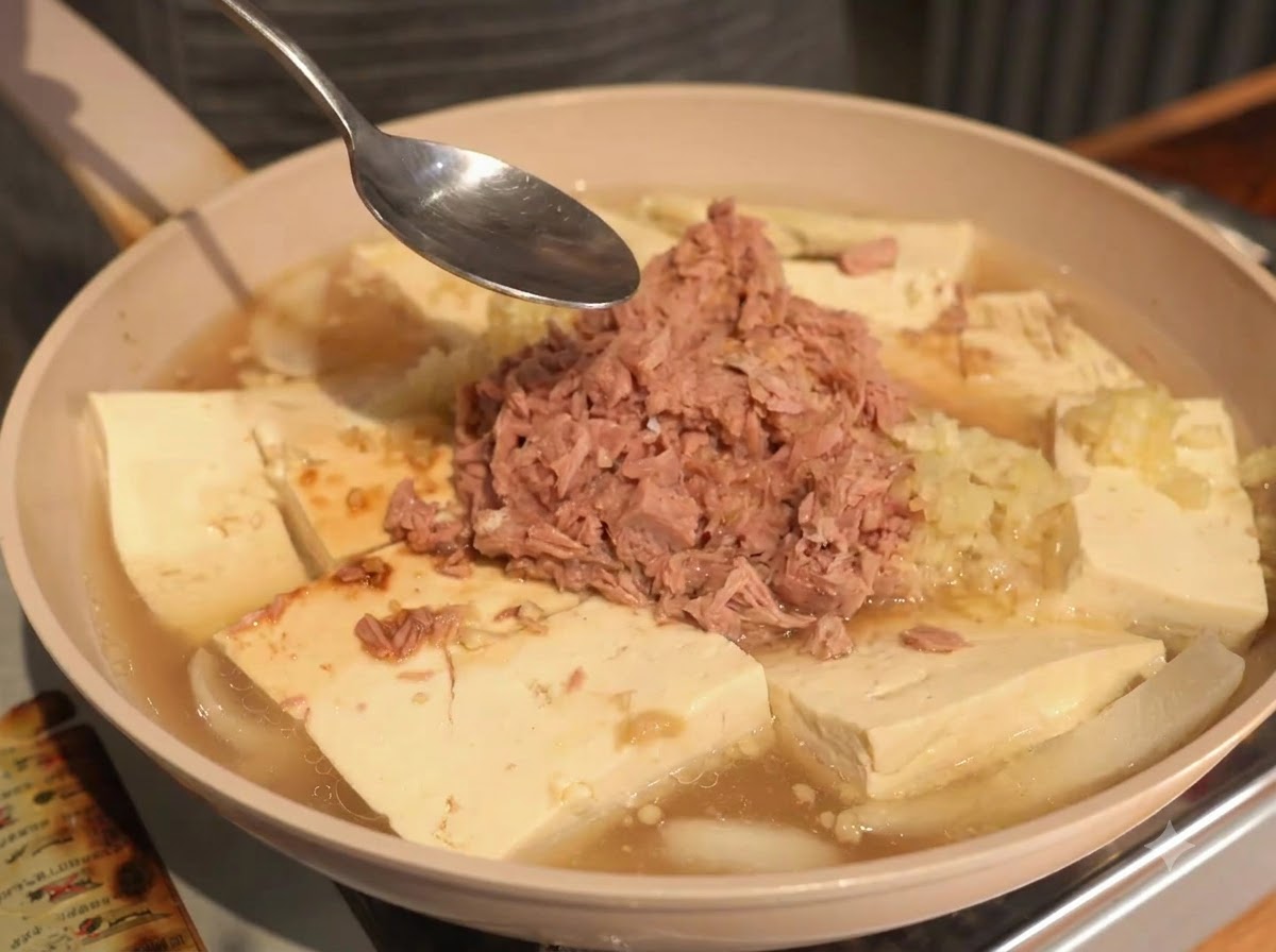 調味料を加える際、ツナ、豆腐、スープの入った鍋の上にスプーンが差し出されている様子。
