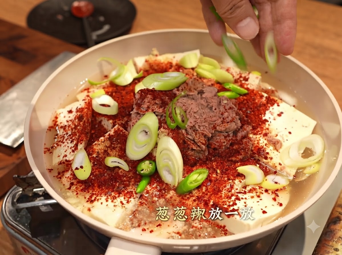 粗挽き赤唐辛子、豆腐、ツナが入った鍋の上に、スライスした長ネギと青唐辛子を両手で散らしている様子。
