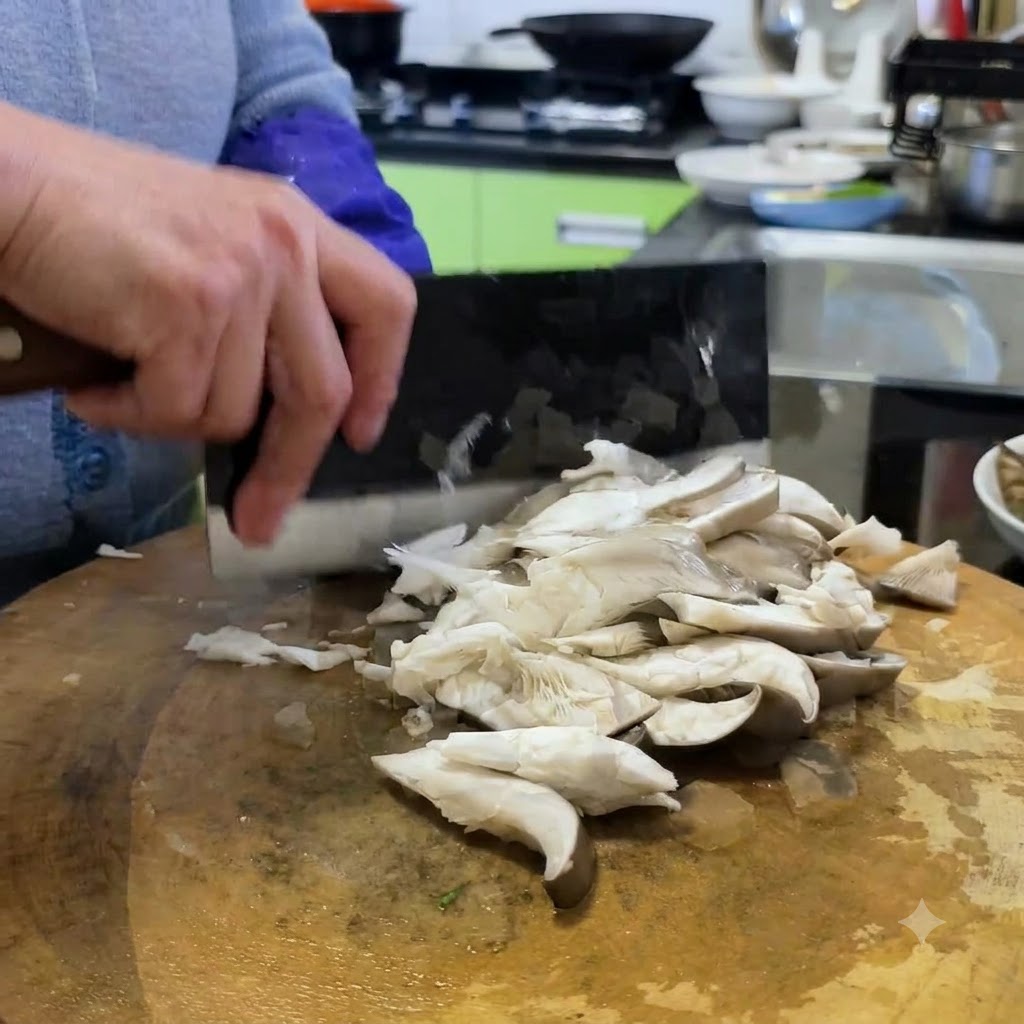 中華包丁を使い、木のまな板の上でひらたけを小さめの食べやすい大きさに切っている様子。