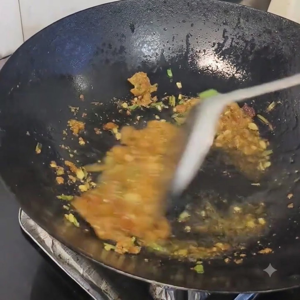 熱した中華鍋の中で、炒めた香味野菜に豚のラードかすを混ぜ合わせている様子。