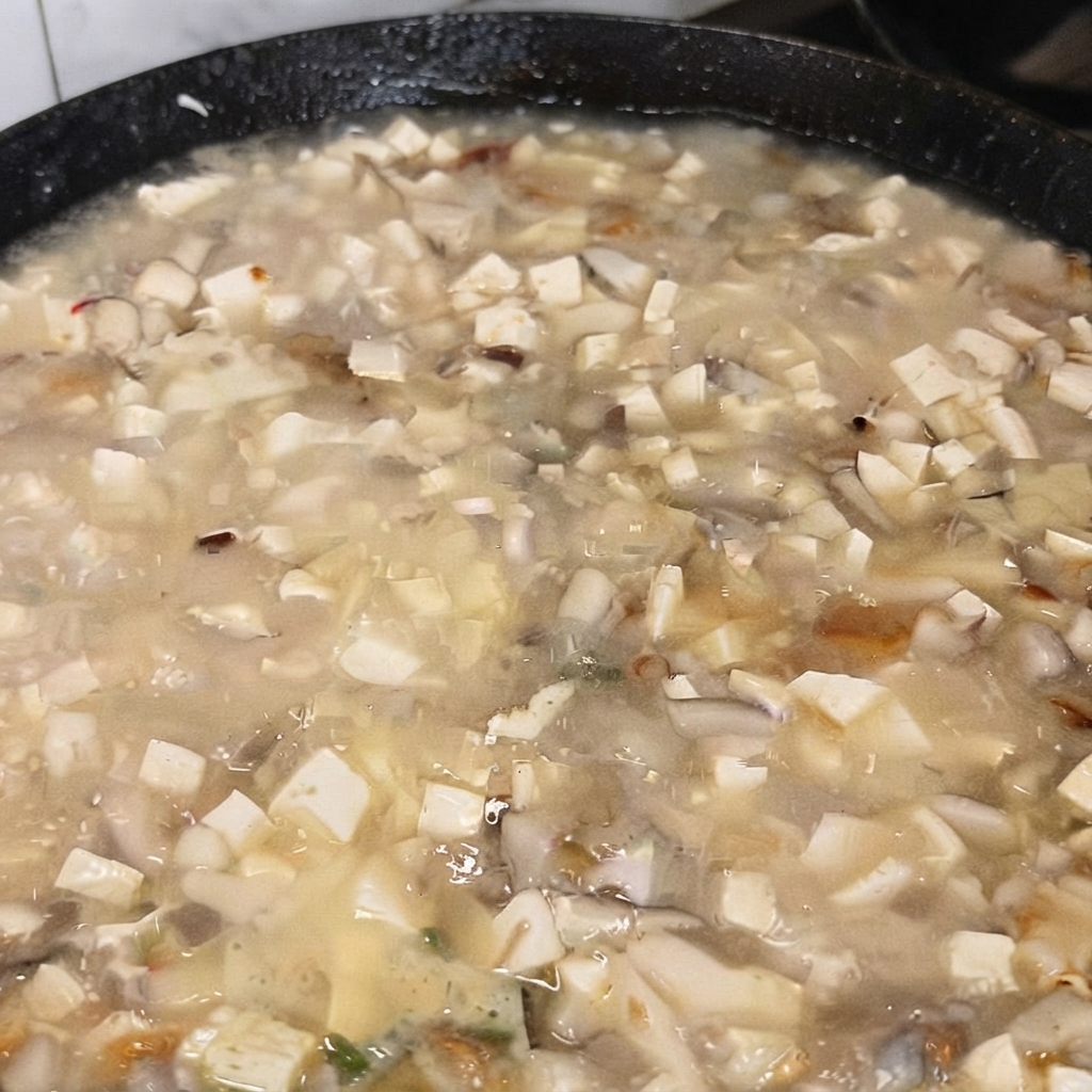 沸騰している豆腐スープに、うま味調味料をスプーンですくい入れている様子。