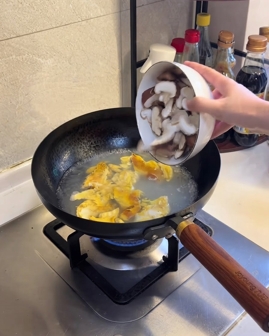 沸騰したお湯と卵の混合液にスライスした椎茸を加えている様子。