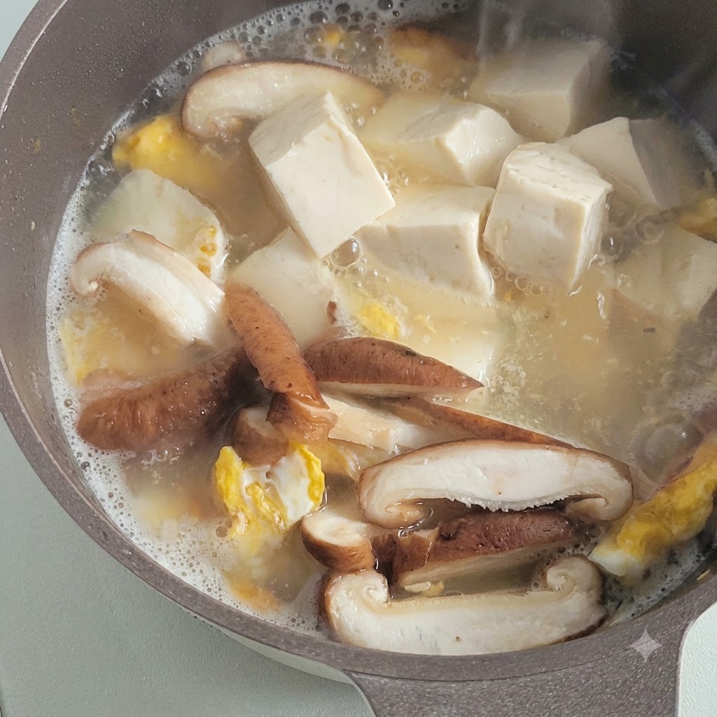 スライスしたきのこや炒り卵と一緒に、さいの目切りにした白い豆腐がスープで煮込まれている様子