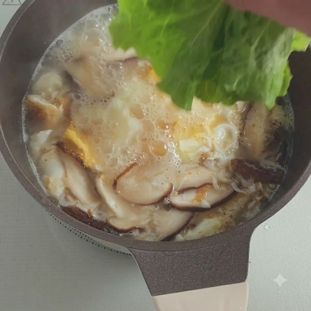 きのこと卵の入った沸騰した鍋に、新鮮なレタスの葉を入れている様子
