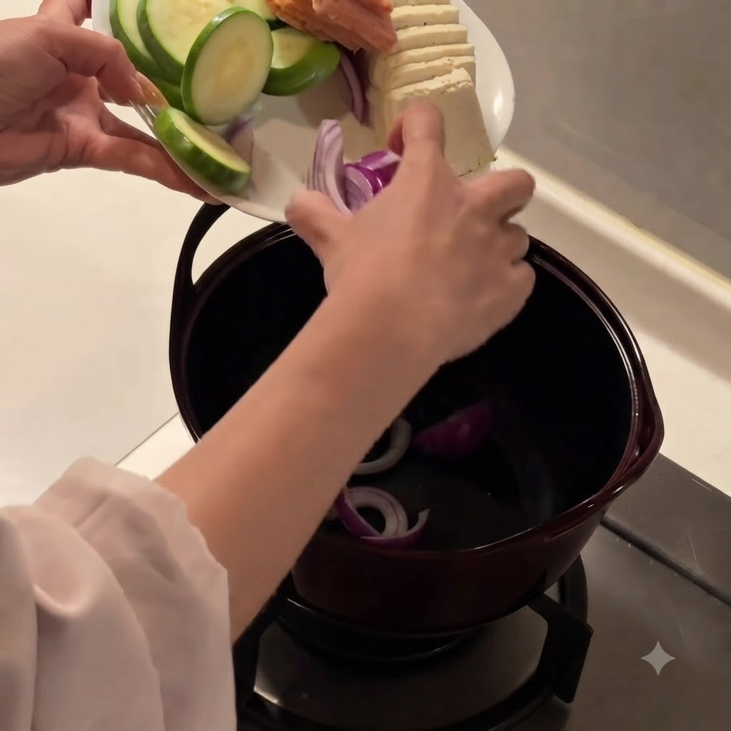 黒い調理鍋の底に、スライスした赤玉ねぎを入れている様子。