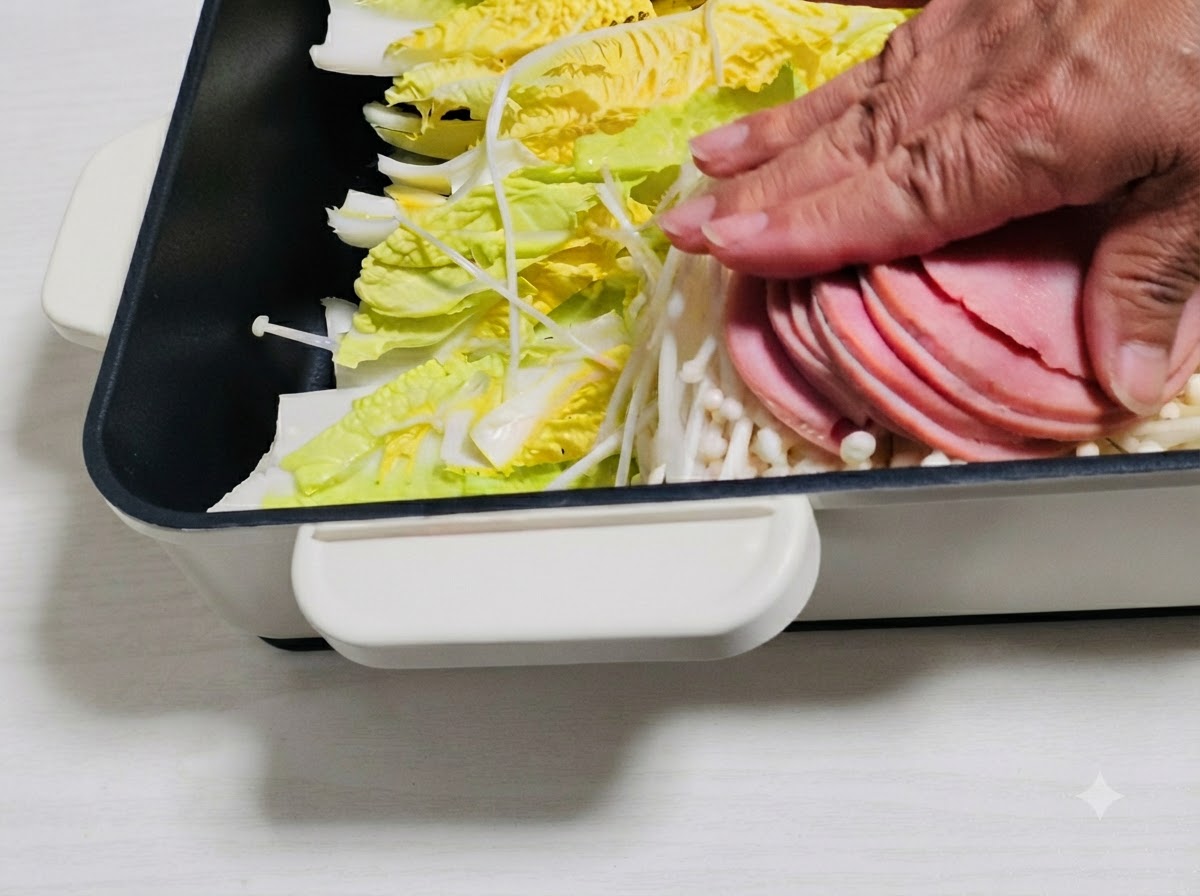 鍋の中の野菜の上にハムのスライスなどの具材を並べている様子。