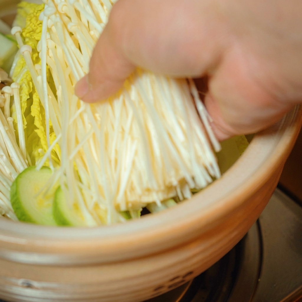 新鮮なエノキタケを鍋の中の野菜の上に置いている様子。