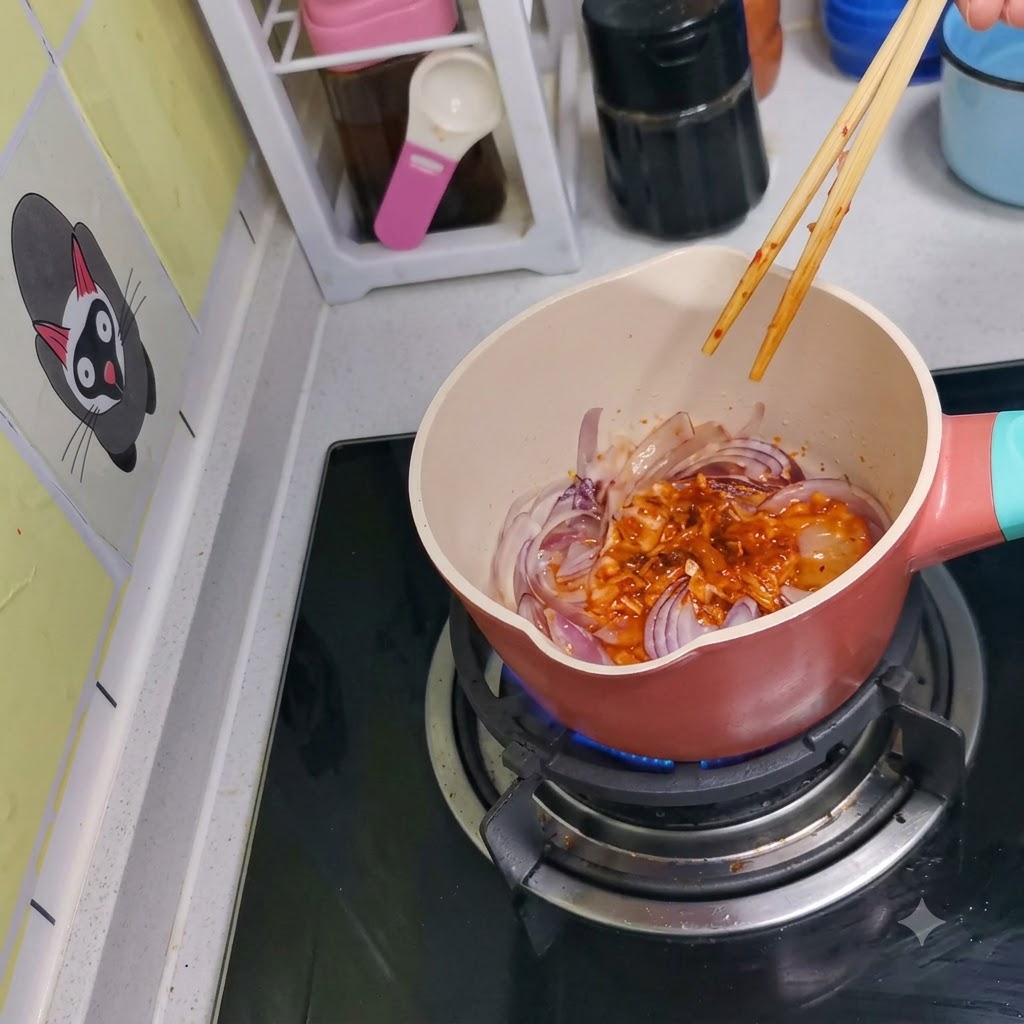 木製の箸を使って、鍋の中でキムチと赤玉ねぎが一緒に炒められている様子。