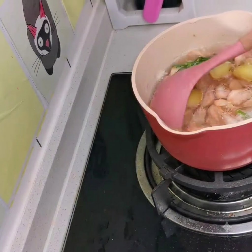 ピンク色のスパチュラを使って、韓国風ラーメンの煮込み鍋に小エビが混ぜ込まれている様子。