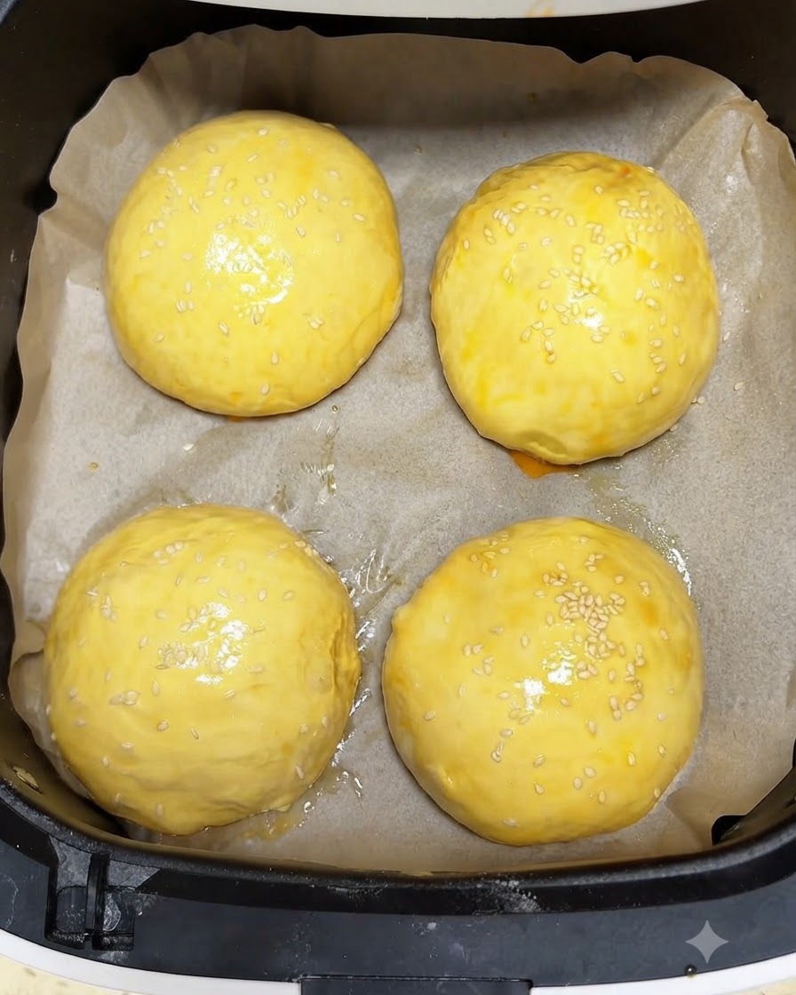 ノンフライヤーのバスケット内で、卵液を塗り白ごまをトッピングした4つの黄金色の生地が焼き上げを待っている様子。