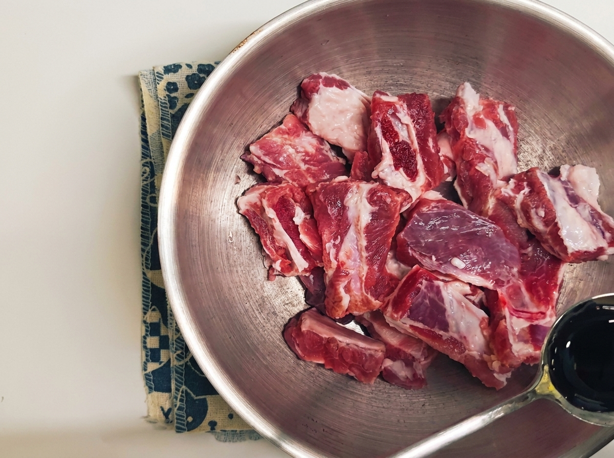 スプーンを使って生肉の上に濃い色の液体調味料を注いでいる様子。cite: 1