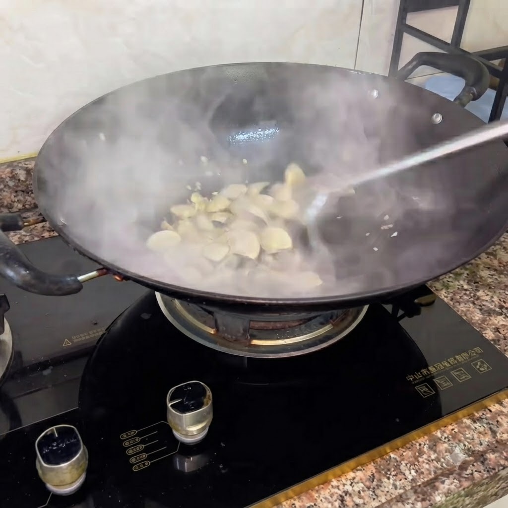 炒めている最中の湯気が立つ白ハマグリの鍋に、料理酒を加えている様子