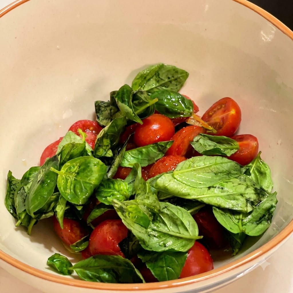 白いボウルに入った味付けされたチェリートマトの上に、緑色のフレッシュバジルの葉が山積みにされている様子