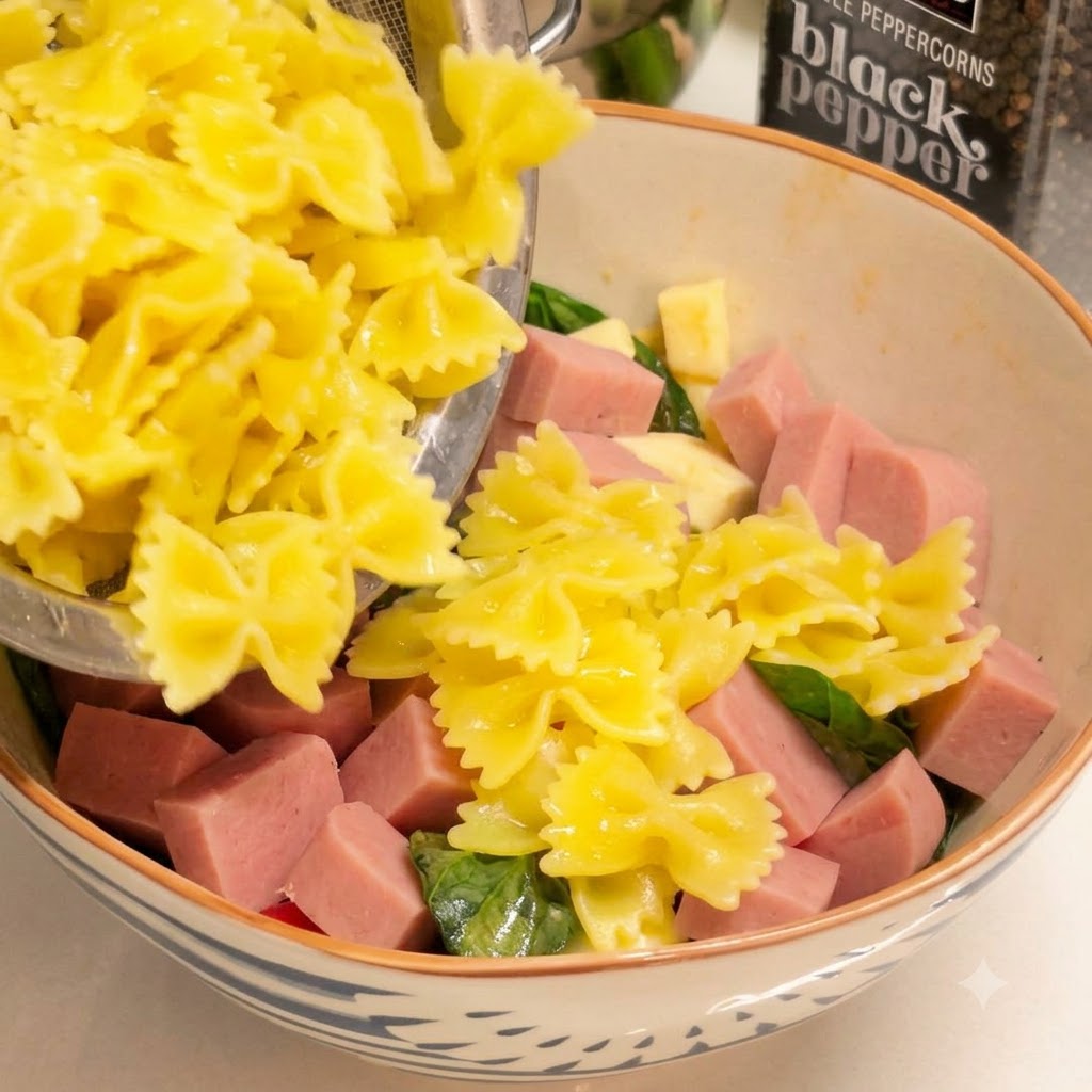 茹で上がった黄色のファルファッレパスタをザルにあけ、角切りハムやグリーンが入ったボウルに移し替えている様子