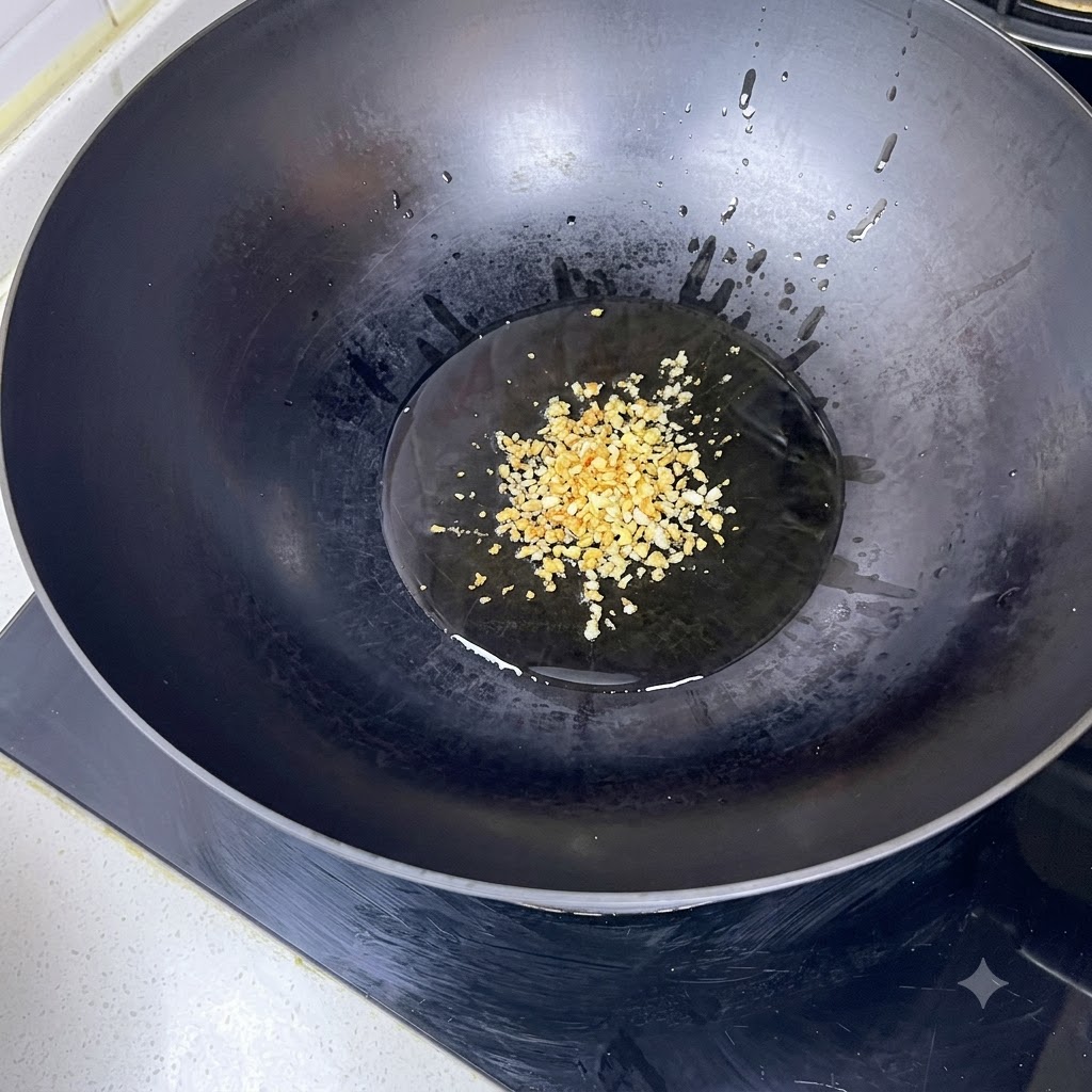黒い中華鍋の中で熱した油でみじん切りのにんにくを炒めている様子。