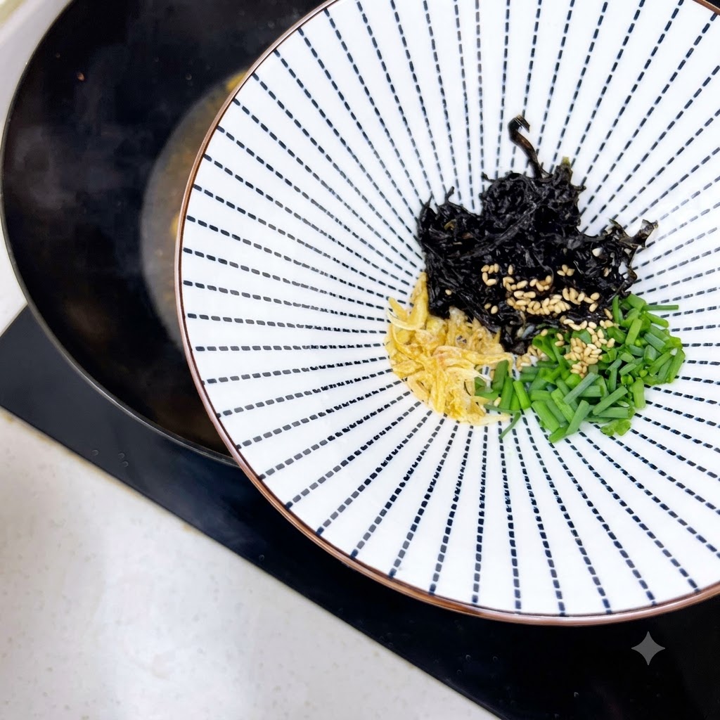 干しエビ、白ごま、青ネギ、海苔が入った器が、火にかけた鍋の隣に置かれている様子。