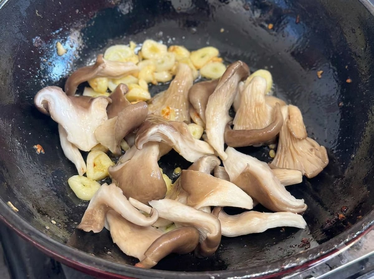 にんにくとねぎが入った中華鍋に加えられる生のひらたけ。