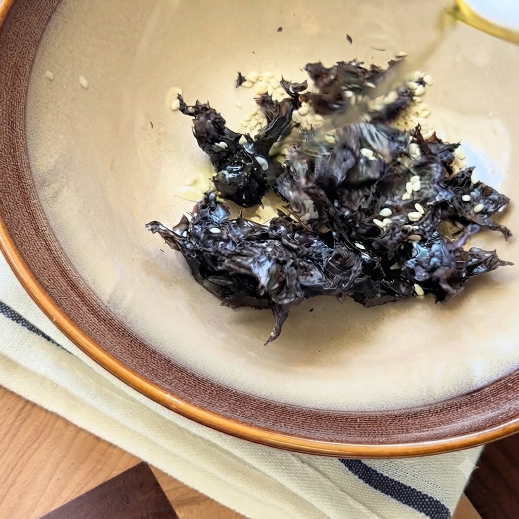 陶器の器の中の乾燥海藻と白ごまにかけられている四川山椒油。