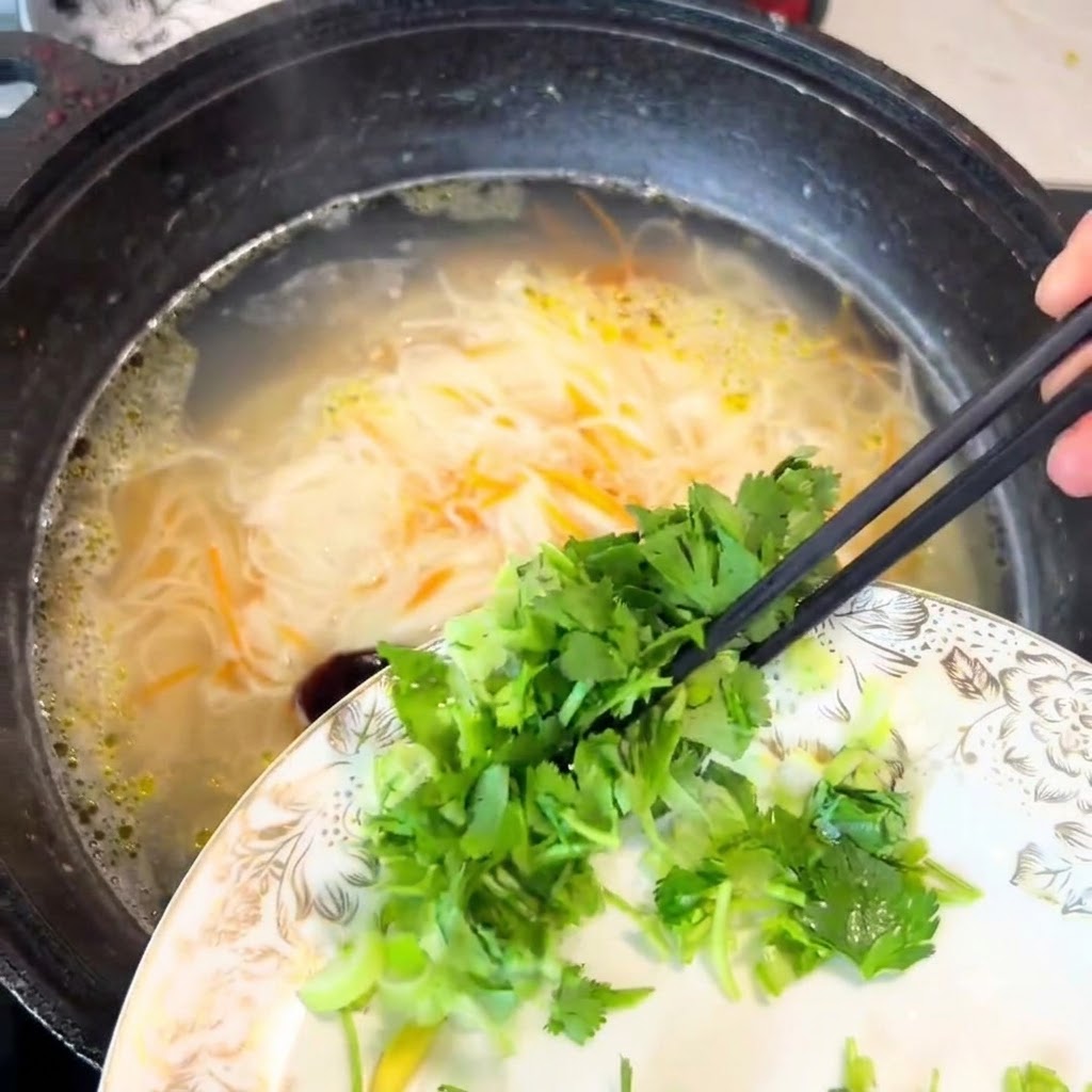 お箸を使ってパクチーと青ねぎを鍋に落とし入れている様子。