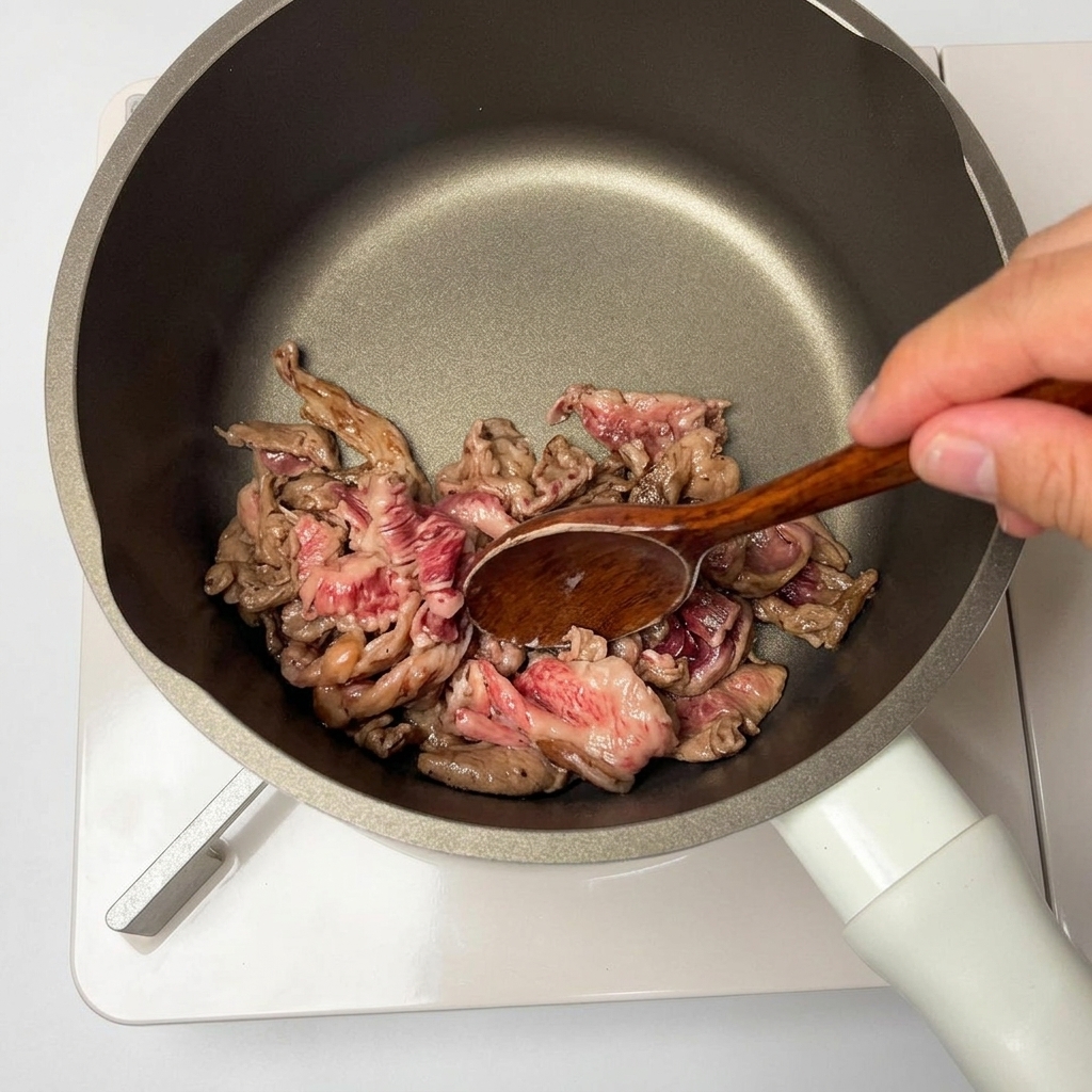 木べらを使ってノンスティック加工のフライパンで下味付きの牛肉スライスを炒めている様子。