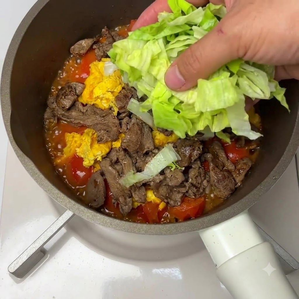 フライパンの中の牛肉、卵、トマトのミックスの上に刻んだレタスが乗せられている様子。